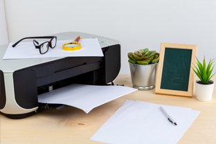 Bild: Tintenstrahldrucker mit Papier am Schreibtisch und nebenbei stehen ein paar grüne Pflanzen